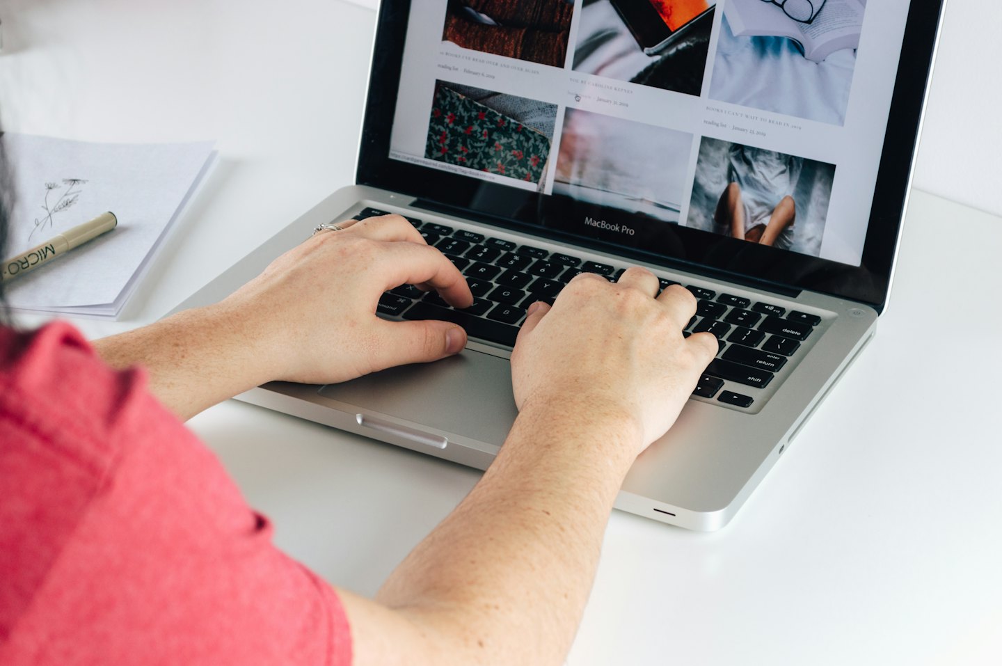 Osoba pisząca na srebrnym laptopie MacBook Pro przy białym biurku.