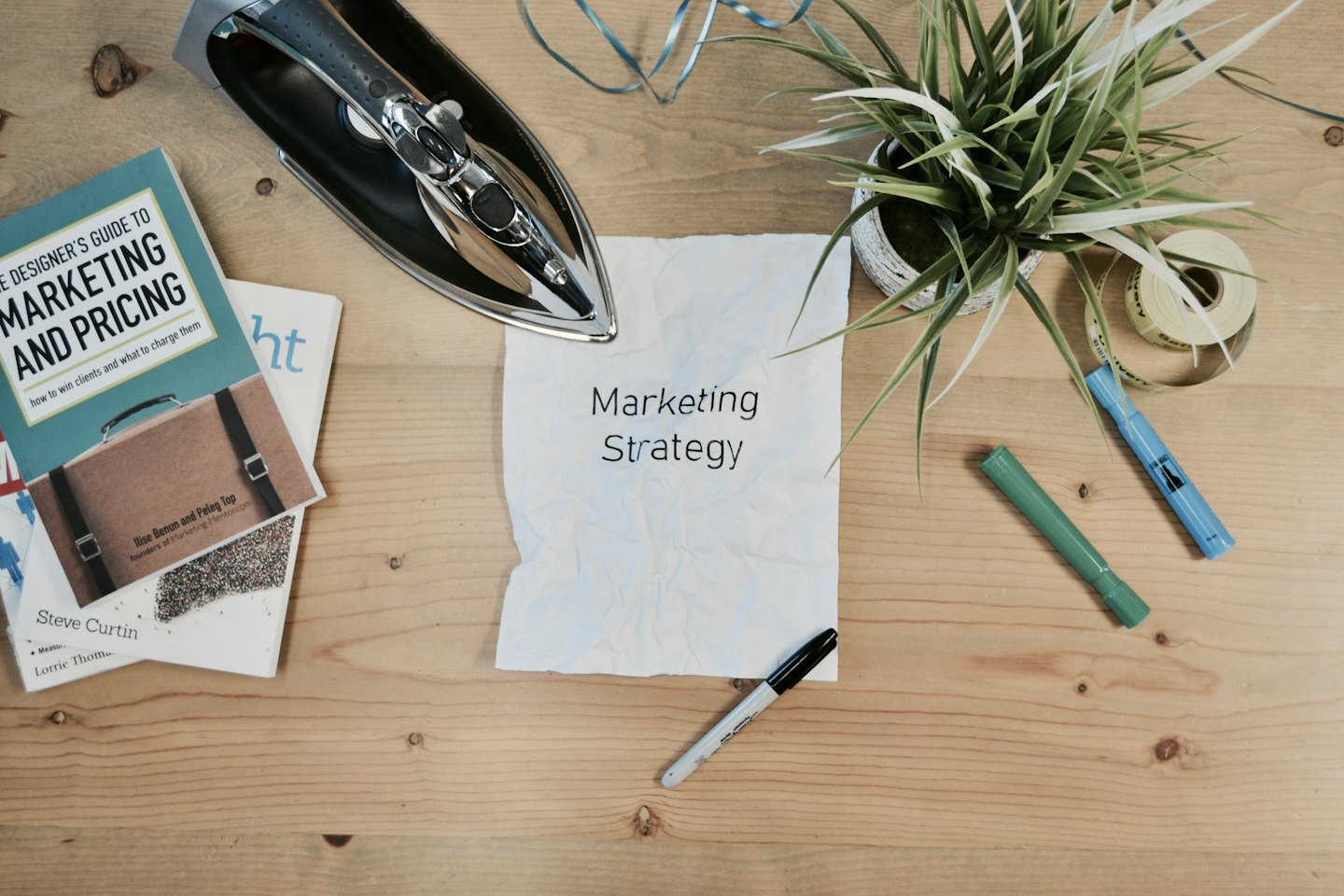 Drewniane biurko z książkami o marketingu i pogniecioną kartką 'Strategia marketingowa'.